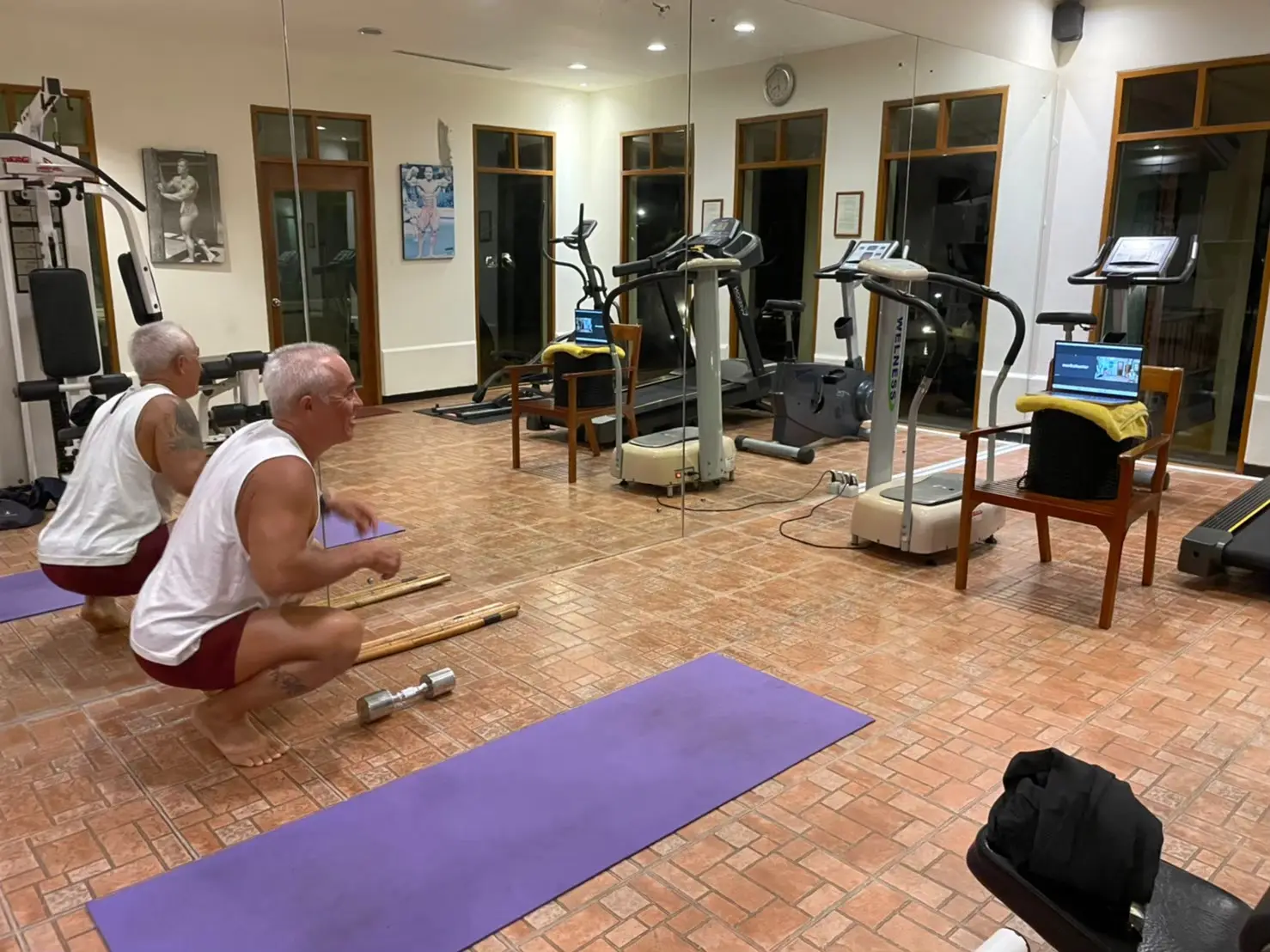 Distance learning fitness training showing client performing squat exercise in home gym following laptop video coaching