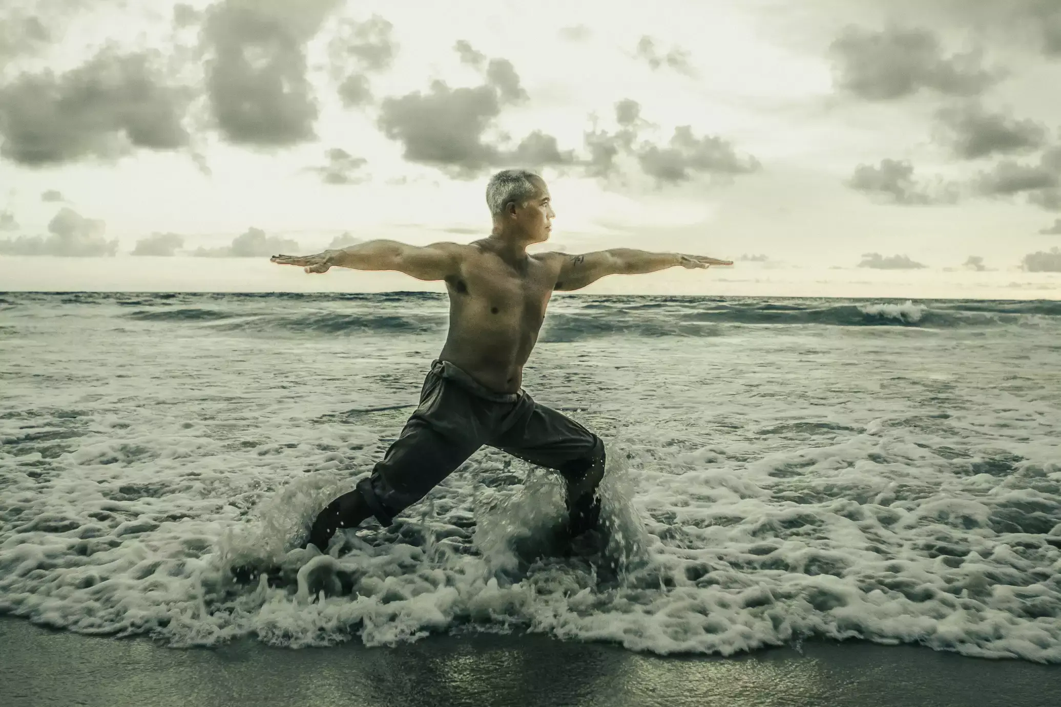 Karol Krauser performing warrior II pose in ocean waves on Phuket beach Thailand