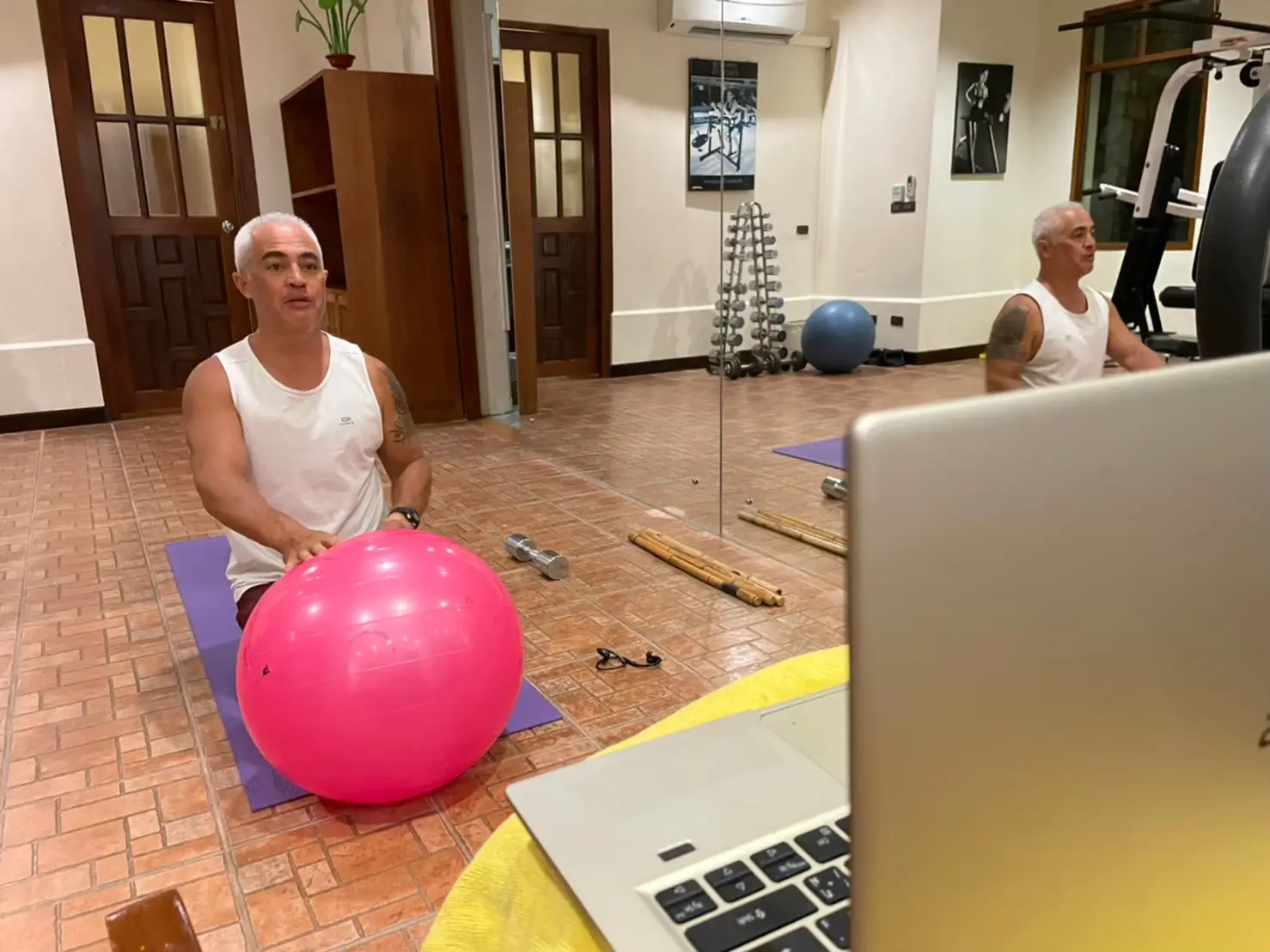 Remote personal training session with stability ball exercise in home gym setting with laptop